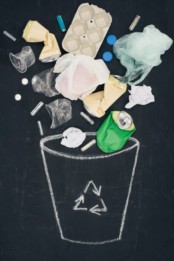 various types of trash falling into drawn trash bin with recycle sign on chalkboard